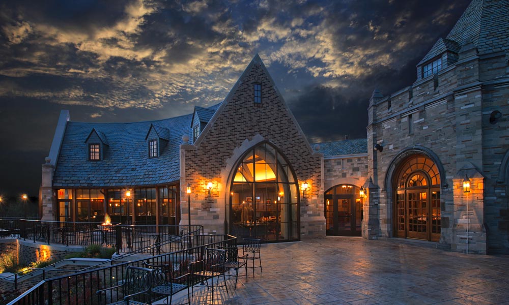 stone-walled private clubhouse at dusk with curved timber frame purlins facing the patio and gothic architecture