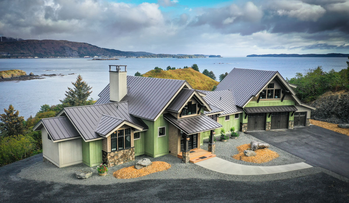 Aerial shot of a large timber home with multiple roof lines, both gable and shed - house sits on the shore with mountains in background