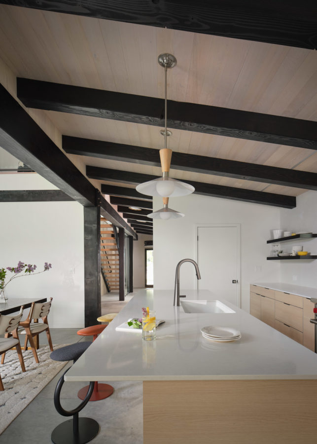 Uncluttered kitchen with wood ceiling, white walls, island with modern stool seating